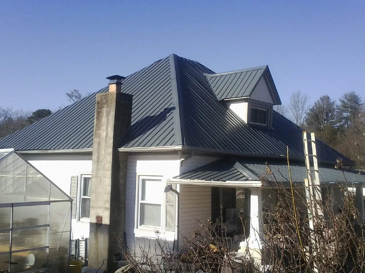Dark blue standing seam metal roof on a white farmhouse with dormer — Slate & Tile Roof Repair by Roofing Brothers in Schofield
