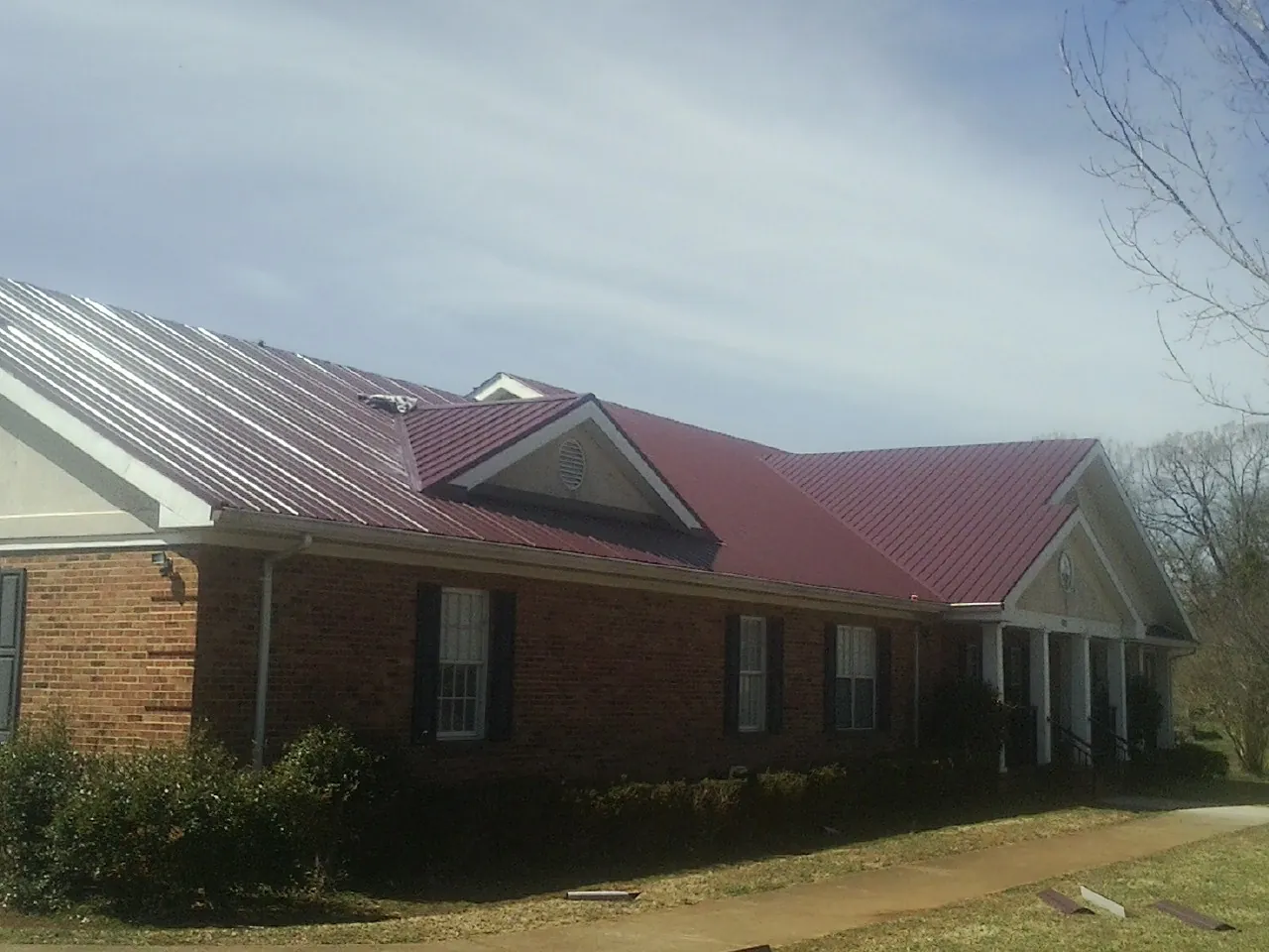 Red metal roof with gabled entries on a long brick building, from a Hail Damage Roof Repair job in Schofield