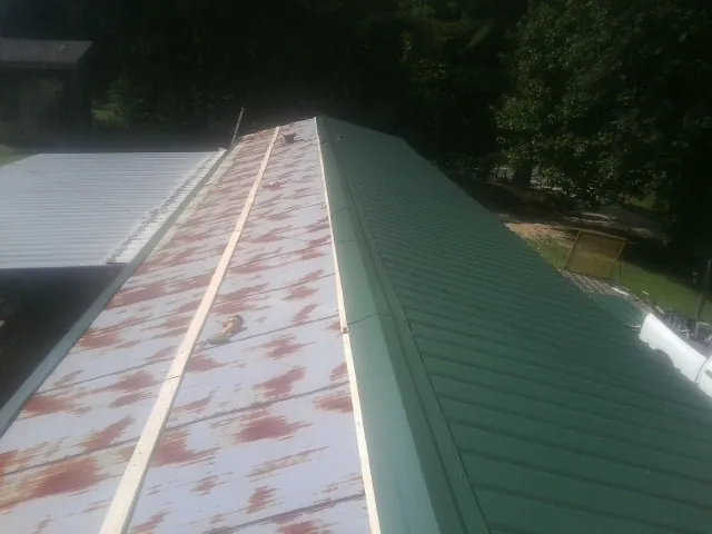 Old rusted panels beside newly installed green metal roofing — Wind Damage Roof Repair by Roofing Brothers in Schofield