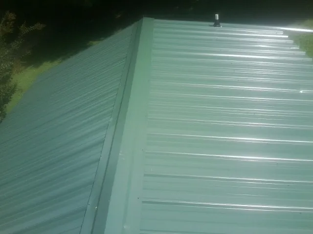 New green metal panels meeting at the ridge of a roof — Flat Roof Repair work by our crew in Schofield