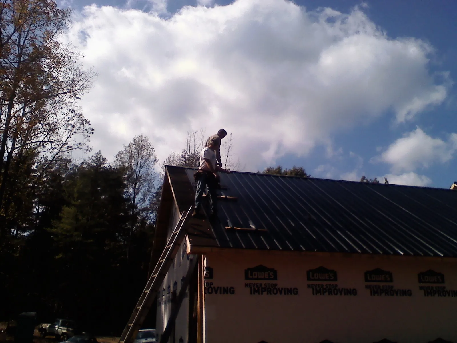 Roofer fastening dark metal panels high against a cloudy sky, from a Roof Inspection job in Schofield